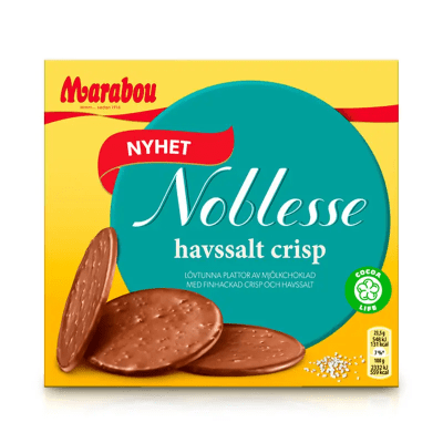Zoom bild av Marabou Noblesse Havssalt Crisp 150g gul ask med teal cirkel, lövtunna mjölkchokladdiskar visas framför förpackningen