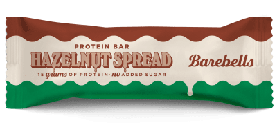 Zoom bild av Barebells Hazelnut Spread proteinbar 45g i förpackning med brun, vit och grön design, med synlig chokladfylld bar bredvid